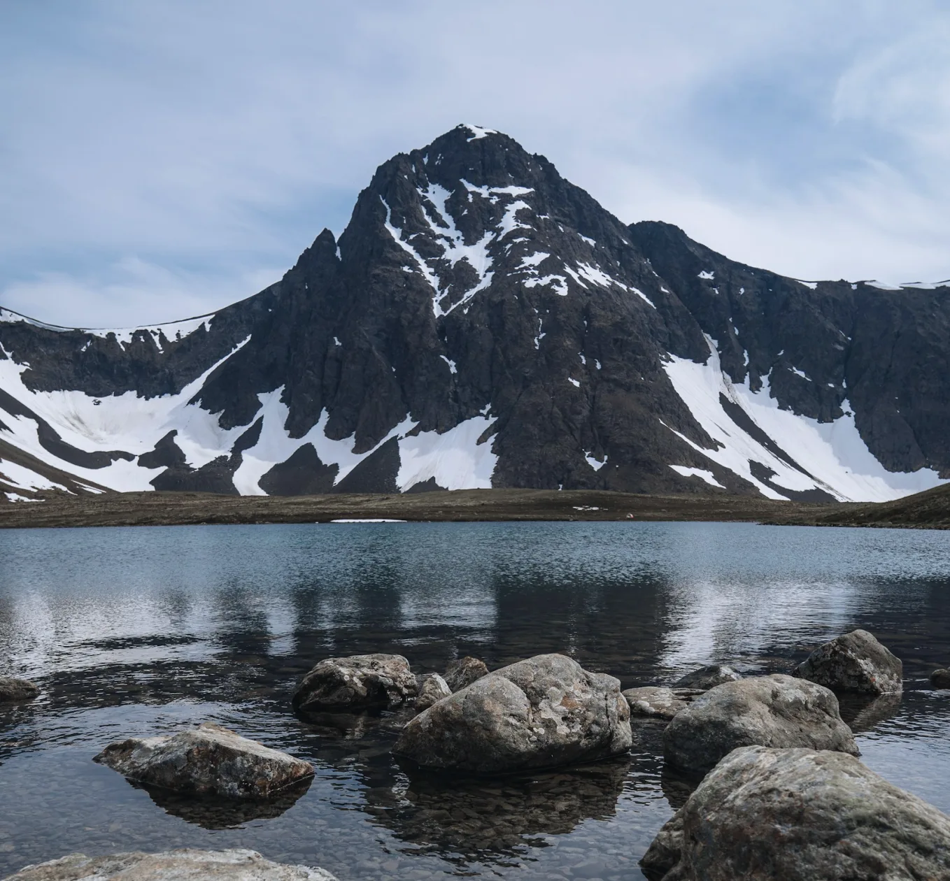 Boulders along a lake shore below a snowy mountain peak